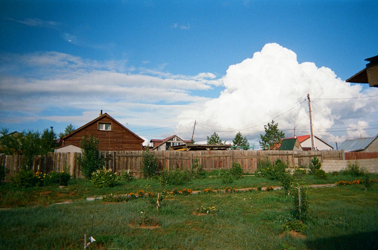 Offerings Picturesque view of a rural village scene with wooden houses, a garden, and a vibrant sky.