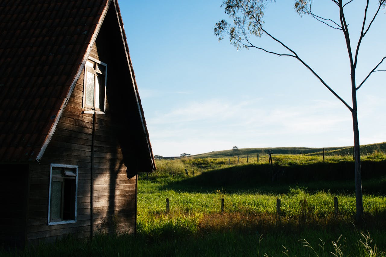 About Charming rustic farmhouse in a sunny rural landscape with lush greenery.
